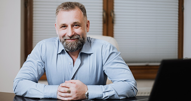 Middle age man with grey beard folding hands in office building